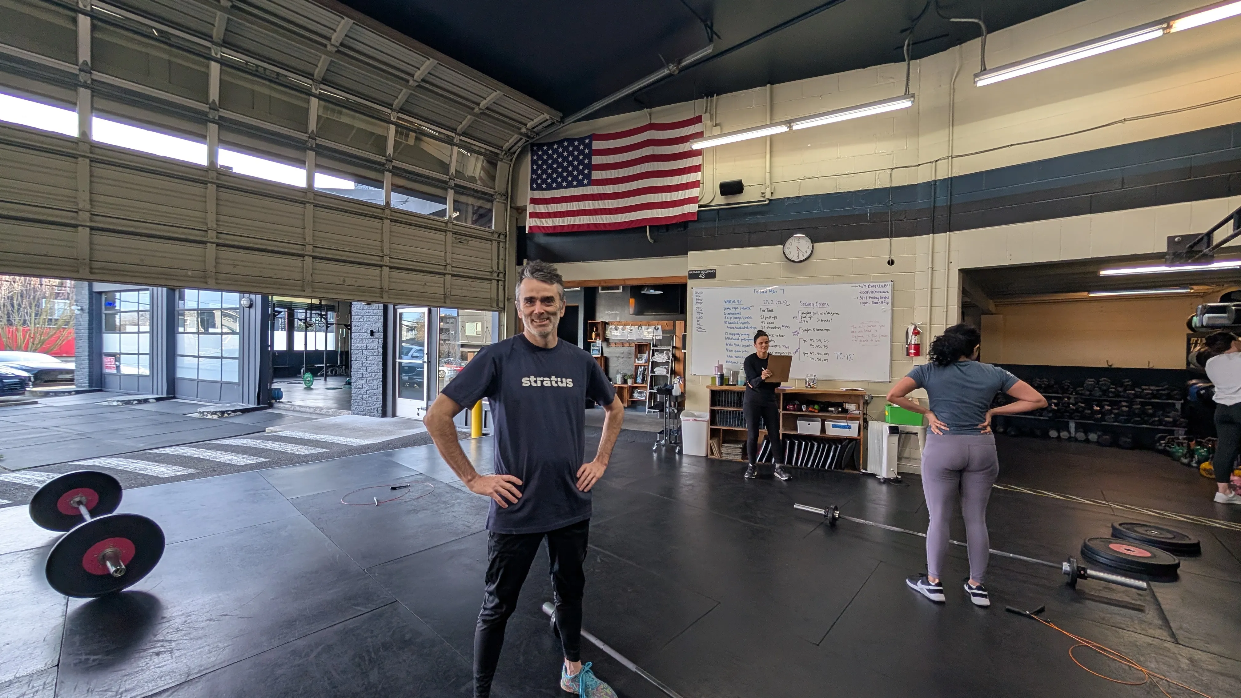 Gene at CrossFit gym wearing Stratus t-shirt with programming whiteboard behind him